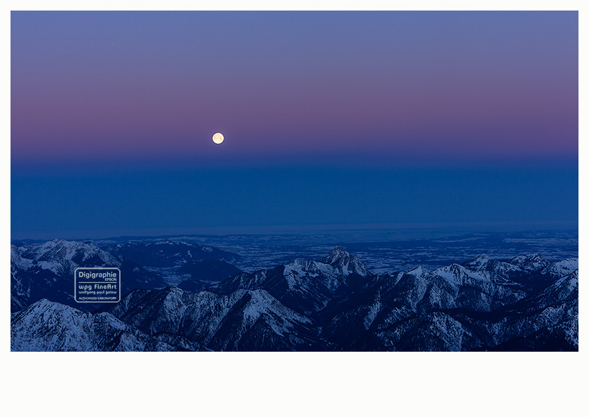 FineArt-Poster und Digigraphie (6): der Vollmond in der Morgendämmerung am blauvioletten Himmel, im Vordergrund verschiedene Berggipfel in Blau und Schwarz, fotografiert vom Gipfel der Zugspitze.